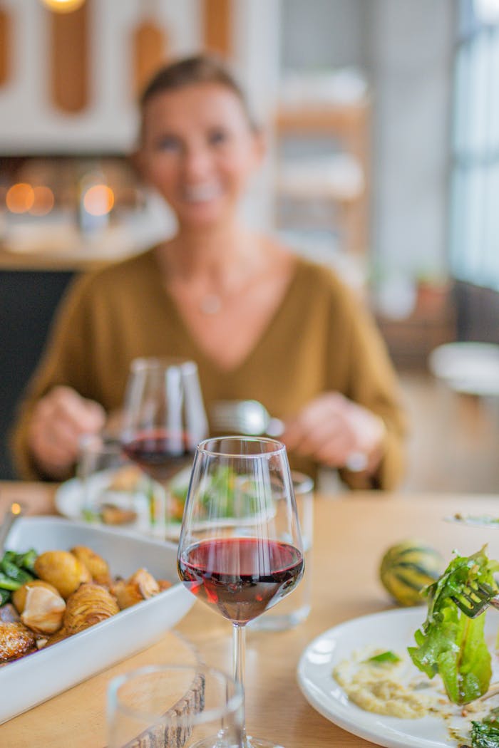 A woman sitting at a cozy dinner table with food and red wine, enjoying a casual meal.