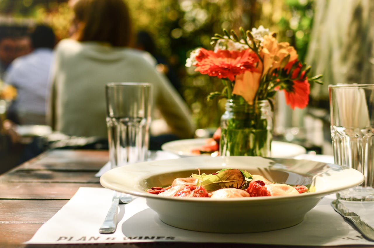 Delight in a cozy outdoor dining scene featuring a beautifully plated pasta dish and floral arrangements.